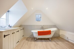 Ein Badezimmer mit einer freistehenden Badewanne, einem Fenster und einem weißen Waschtisch mit Schränken.