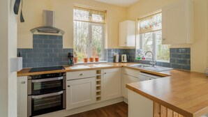Una cucina con forno a incasso, piano cottura, lavello e una finestra vista alberi.