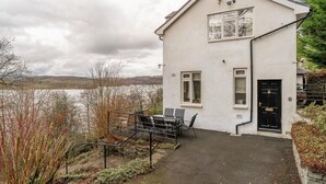 Un edificio a un piano con una porta nera, un piccolo portico con tavolo e sedie, e vista su un lago.