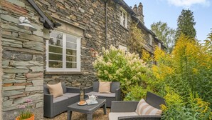 A stone building with a window, outdoor seating area with wicker furniture, and a variety of plants. - 3 Bed in Skelwith Bridge (oc-lr033) (Skelwith)