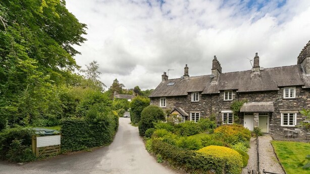 A stone cottage with a paved driveway leading to a gated entrance, surrounded by lush greenery. - 3 Bed in Skelwith Bridge (oc-lr033) (Skelwith)