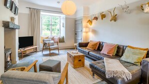 A living room with a sofa, armchairs, a television, a fireplace, and a large window. - 3 Bed in Skelwith Bridge (oc-lr033) (Skelwith)