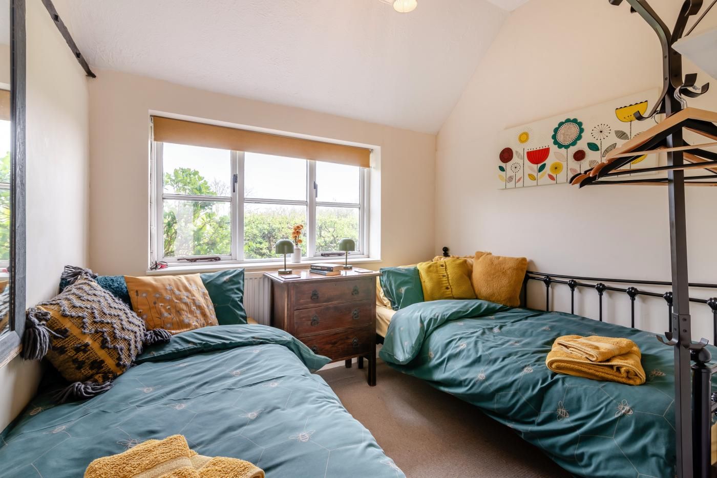 A room with two beds, a window, a dresser, and a wall-mounted rack.