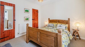 Ett sovrum med en säng i trä, två sänglampor, en spegel och en dörr med en röd ram.