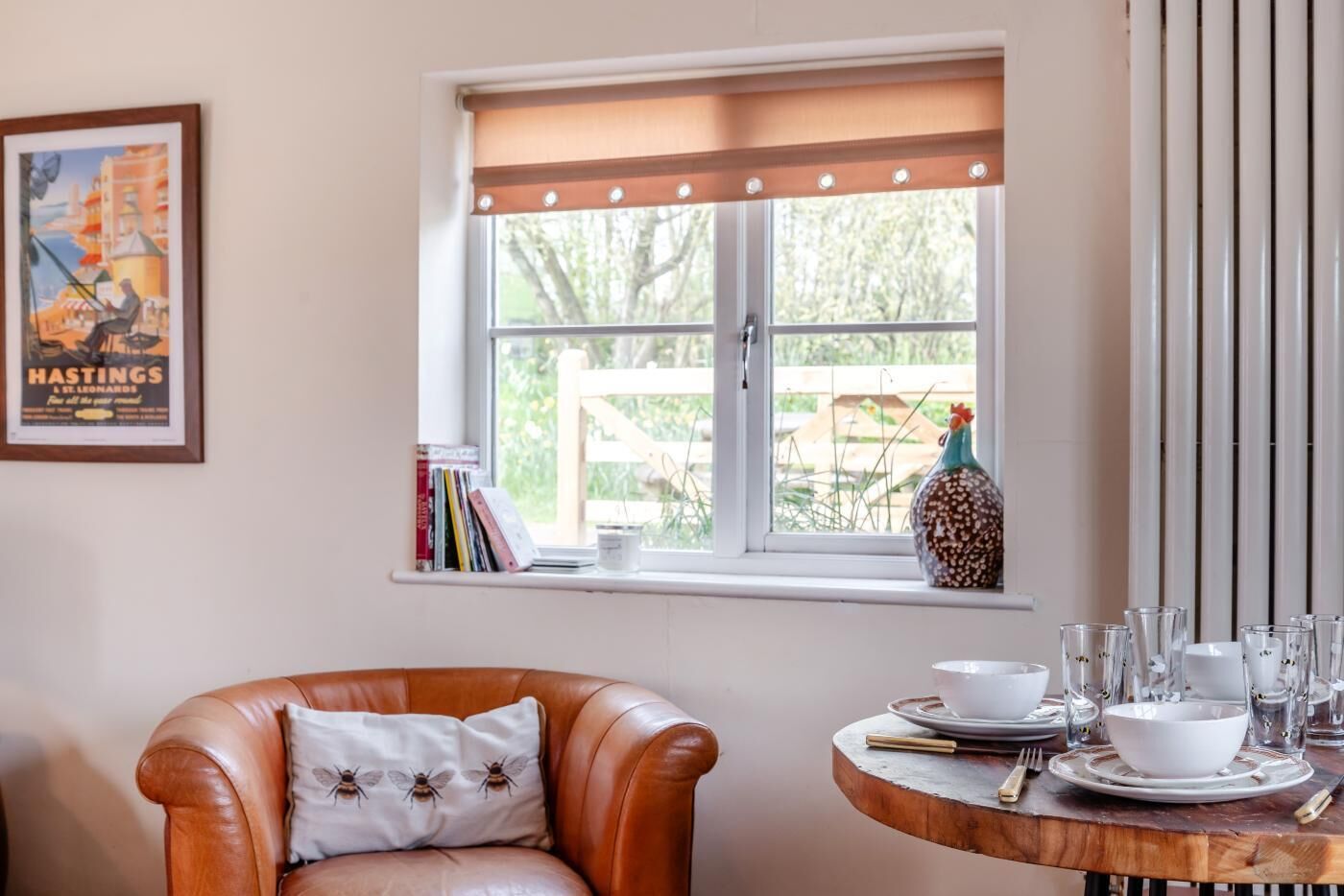A room with a window, a brown leather chair, a small round table with a white bowl and glasses, and a decorative vase.