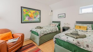 Een slaapkamer met twee bedden, een stoel, een vloerkleed en een schilderij aan de muur.