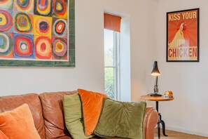 Ein Wohnzimmer mit Ledersofa, farbenfroher Kunst, einem Plakat und einer Lampe auf einem Beistelltisch.