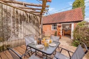 Eine Terrasse mit Frühstückstisch, eine Holzterrasse und ein Backsteinhaus im Hintergrund.