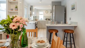 Una cocina moderna con gabinetes blancos, un comedor con mesa dispuesta para dos personas y vistas al área de estar.