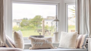 Asiento junto a la ventana con vista a follaje, un farol y un cojín con la inscripción 'Happy Place'.