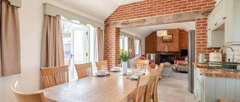 A spacious dining area with a brick archway leading to a kitchen, wooden furniture, and a view of the outdoors.