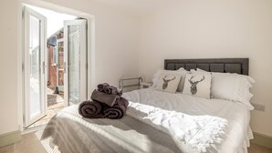 Quarto com cama, almofadas, mesa de cabeceira e vista através de uma porta de vidro.