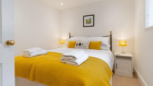 A neatly made bed with a yellow quilt, white pillows, and two bedside lamps. - 1 Bed in Ambleside (oc-lr077) (Ambleside)