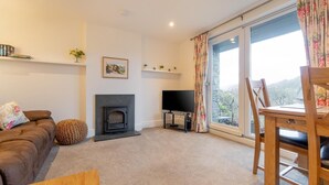 A living room with a sofa, a fireplace, a TV, and a dining area with a table and chairs. - 1 Bed in Ambleside (oc-lr077) (Ambleside)