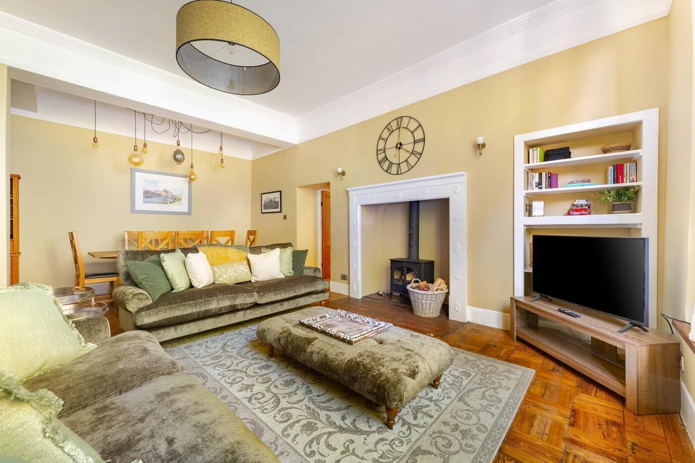 A living room with a sofa, ottoman, TV stand, fireplace, bookshelf, and hanging light fixtures.