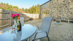 A patio area with a round glass table, a chair, a bottle of wine, and a vase with flowers. - 2 Bed in Easington (oc-coq114) (Easington)