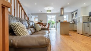 Uma sala de estar ampla com sofá de couro, escada de madeira e cozinha com ilha central.