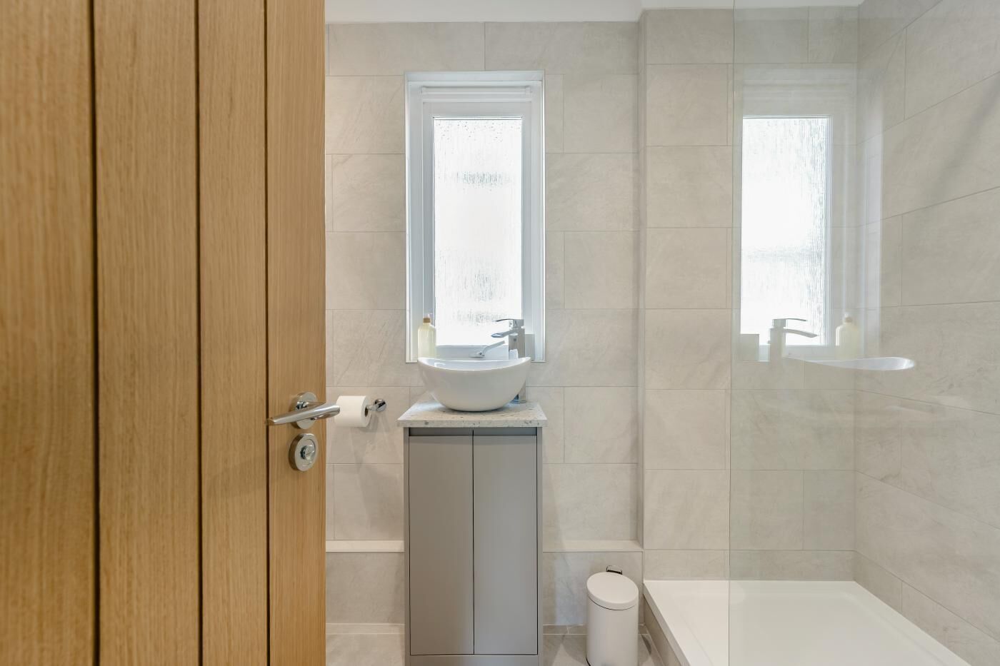 A modern bathroom with a wooden door, a white sink, a toilet, and a bathtub.