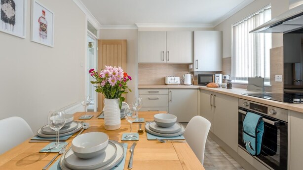 Een moderne keuken met witte kasten, een houten eettafel gedekt voor vier personen en een ingebouwde oven.