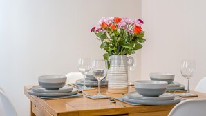 Een eettafel gedekt met borden, kommen en wijnglazen, een vaas met bloemen en een karaf.