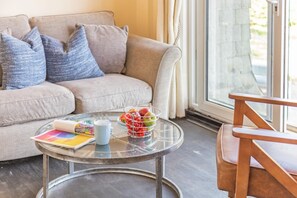 Ein Wohnzimmer mit einer Couch, einem Glastisch, einem Sessel und einem Fenster mit Vorhängen.