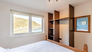 A bedroom with a large window, a bed, a wooden wardrobe, and a framed picture on the wall. - 1 Bed in Lamorna Cove, (oc-h40239) (Lamorna)