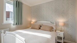 Una camera da letto con un letto, due comodini, una finestra con tende e carta da parati decorata.