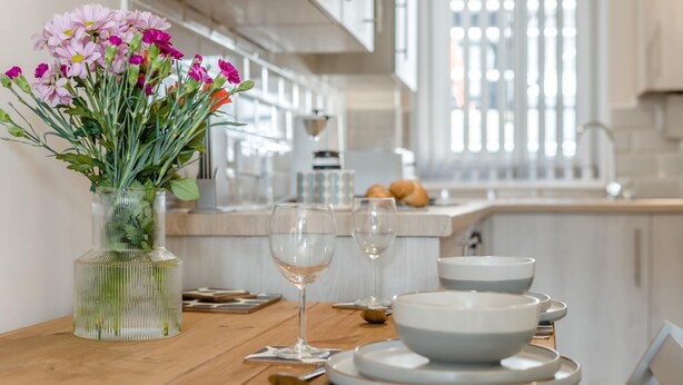 Un tavolo da pranzo con un vaso di fiori, bicchieri da vino e piatti in una cucina moderna.