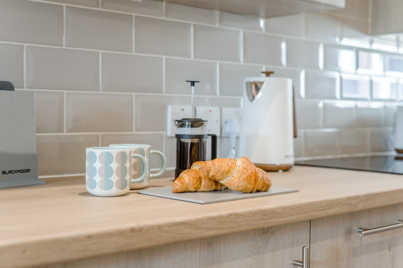 Eine Küchenarbeitsplatte mit Kaffeemaschine, zwei Tassen und einem Croissant.
