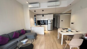 A modern apartment with a grey sofa, a round coffee table, a dining area with a white table and chairs, a kitchen with white cabinets and a refrigerator, and two air conditioning units on the ceiling. - Star Residence Klcc By JR Kuala Lumpur (Kuala Lumpur)