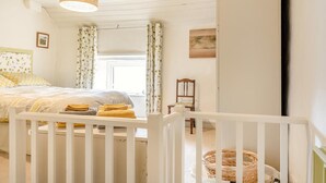 A bedroom with a bed, a crib, a chair, a hanging light fixture, and a window with curtains. - 2 Bed in Buxton (oc-dcbap) (Crowdecote)