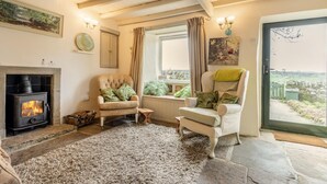 A cozy living room with a fireplace, two armchairs, a large window with a view, and a stone floor. - 2 Bed in Buxton (oc-dcbap) (Crowdecote)