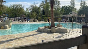 Une piscine bordée de palmiers, une terrasse en bois et un poste de surveillance pour les sauveteurs.