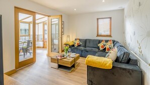 A modern living room with a sofa, coffee table, and a dining area with chairs. - 3 Bed in Pitlochry (oc-t37864) (Pitlochry)