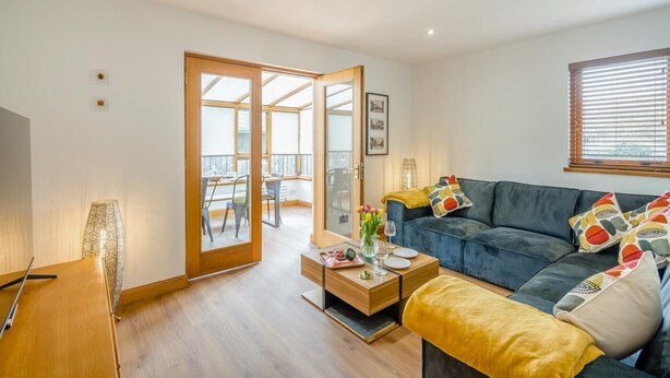 A modern living room with a sofa, coffee table, and a dining area with chairs. - 3 Bed in Pitlochry (oc-t37864) (Pitlochry)