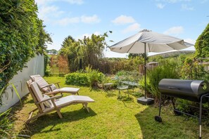 Ein Garten mit Grill, zwei Liegestühlen, einem Tisch mit Stühlen und einem großen Sonnenschirm.