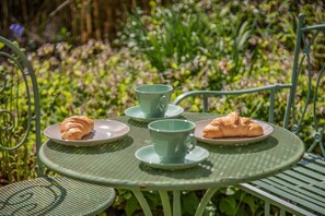 A round metal table with two plates, each holding a croissant and a cup, set outdoors with greenery in the background. - 1 Bed in Upton Cross (oc-c34217) (Caradon Town)