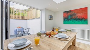 Un coin repas avec une table en bois mise pour le petit-déjeuner, une grande fenêtre et un tableau abstrait aux couleurs vives accroché au mur.