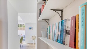 Un couloir avec une bibliothèque remplie de livres, une chaise blanche et une petite table.