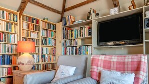 Ein gemütliches Wohnzimmer mit einem karierten Sofa, einem Bücherregal voller Bücher, einer Lampe und einem Fernseher.