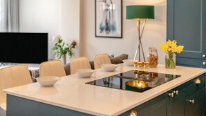 Una cucina moderna con isola centrale, sedie da pranzo, un televisore a schermo piatto, una lampada da terra verde e un vaso con fiori gialli.
