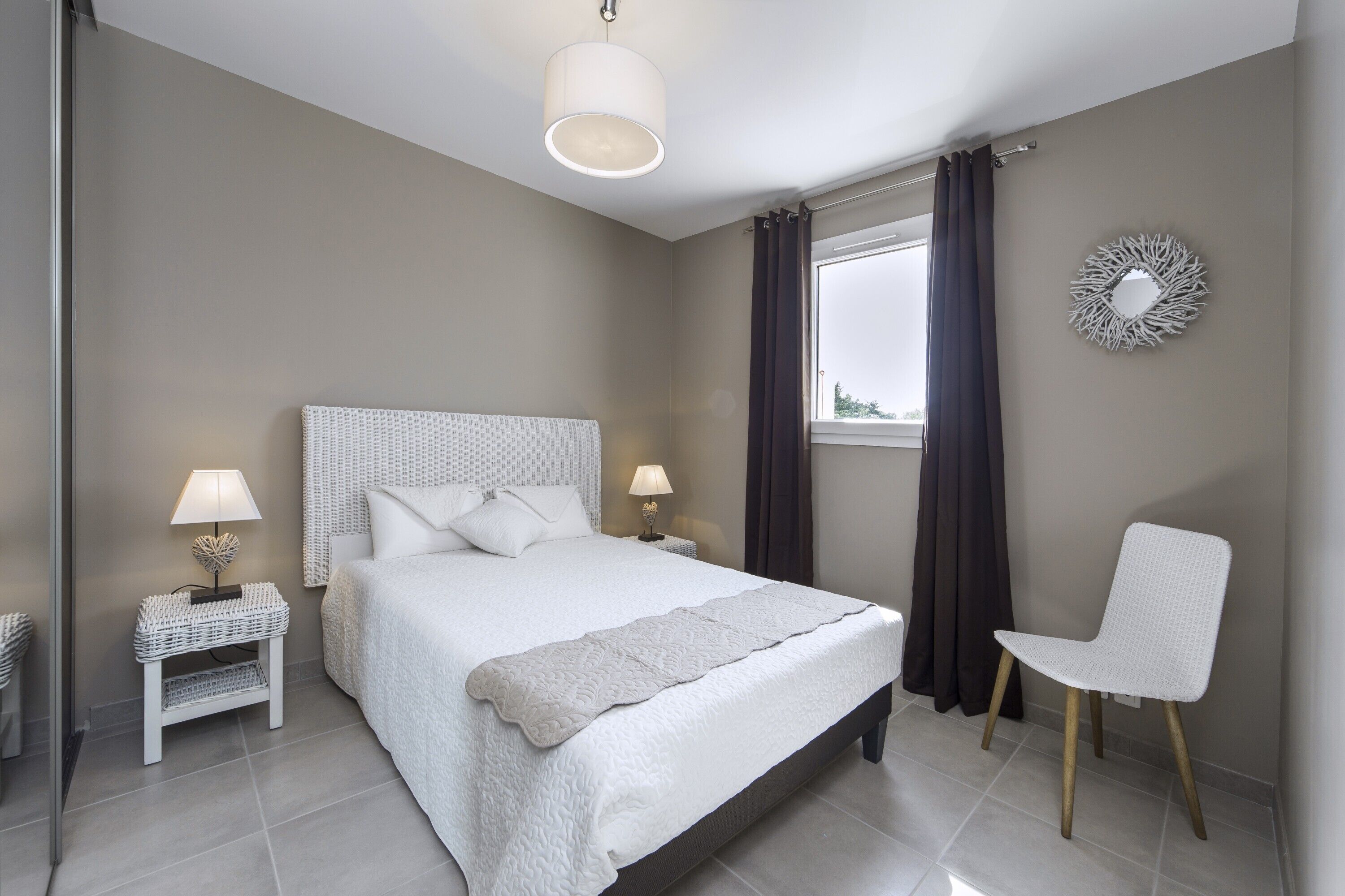 Une chambre à coucher comprenant un lit, des tables de chevet, une chaise, une fenêtre avec des rideaux et un élément de décoration murale.