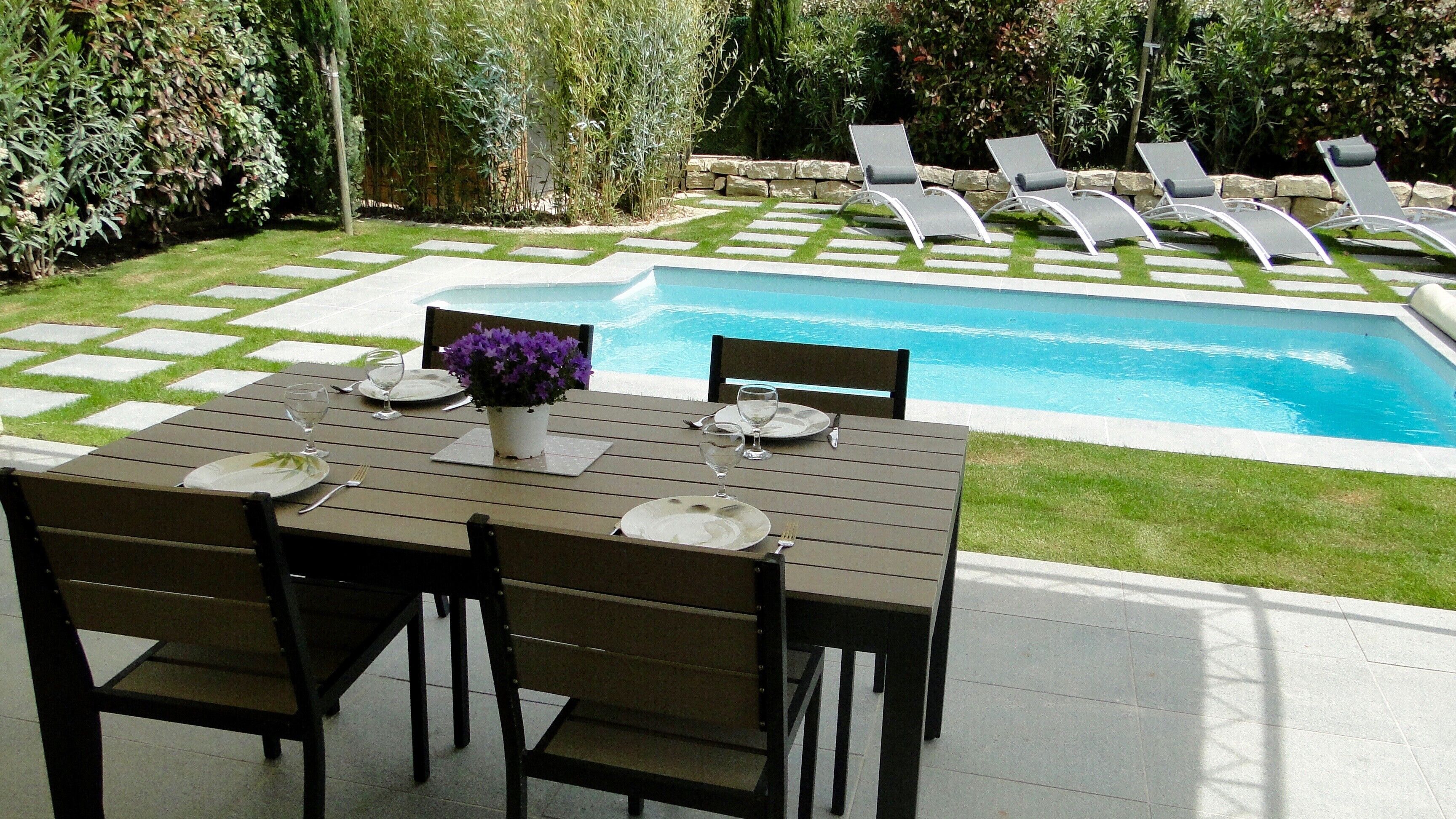 Un espace aménagé au bord de la piscine, avec une table dressée pour les repas, des chaises longues et une vue sur la piscine.