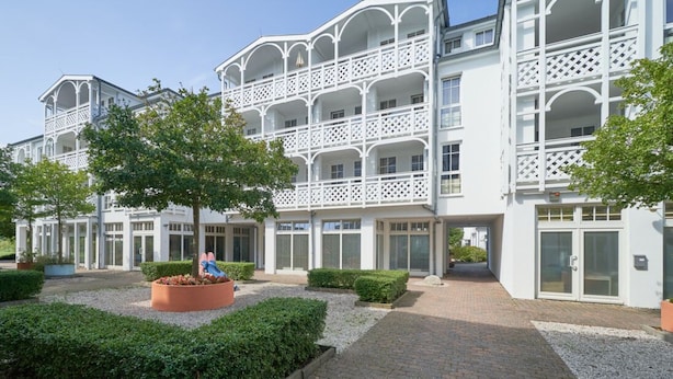 A multi-story hotel with a white facade, balconies, and a landscaped courtyard with hedges and a circular planter. - Exklusive Auszeit an der Ostsee mit Balkon (Sellin)