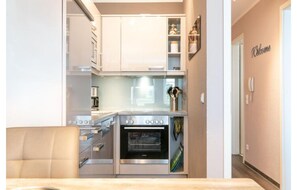 A compact kitchen with a built-in oven, a dining area with a beige chair, and a 'Welcome' sign on the wall. - Exklusive Auszeit an der Ostsee mit Balkon (Sellin)
