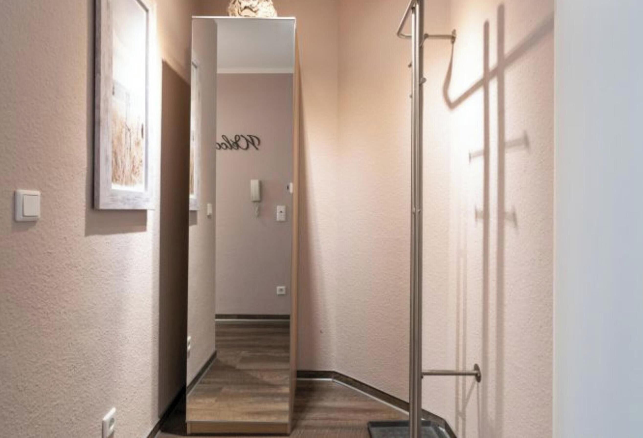 A hallway with a wooden floor, a door at the end, and a wall-mounted light fixture.
