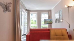 A room with a red sofa, a wooden table, and a painting on the wall. - Exklusive Auszeit an der Ostsee mit Balkon (Sellin)