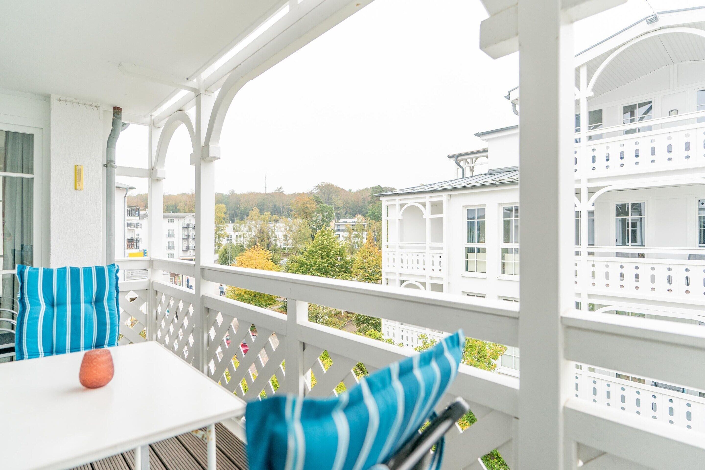 Ein weißer Balkon mit Tisch und Stühlen, Blick auf Gebäude und ein weißer Zaun.