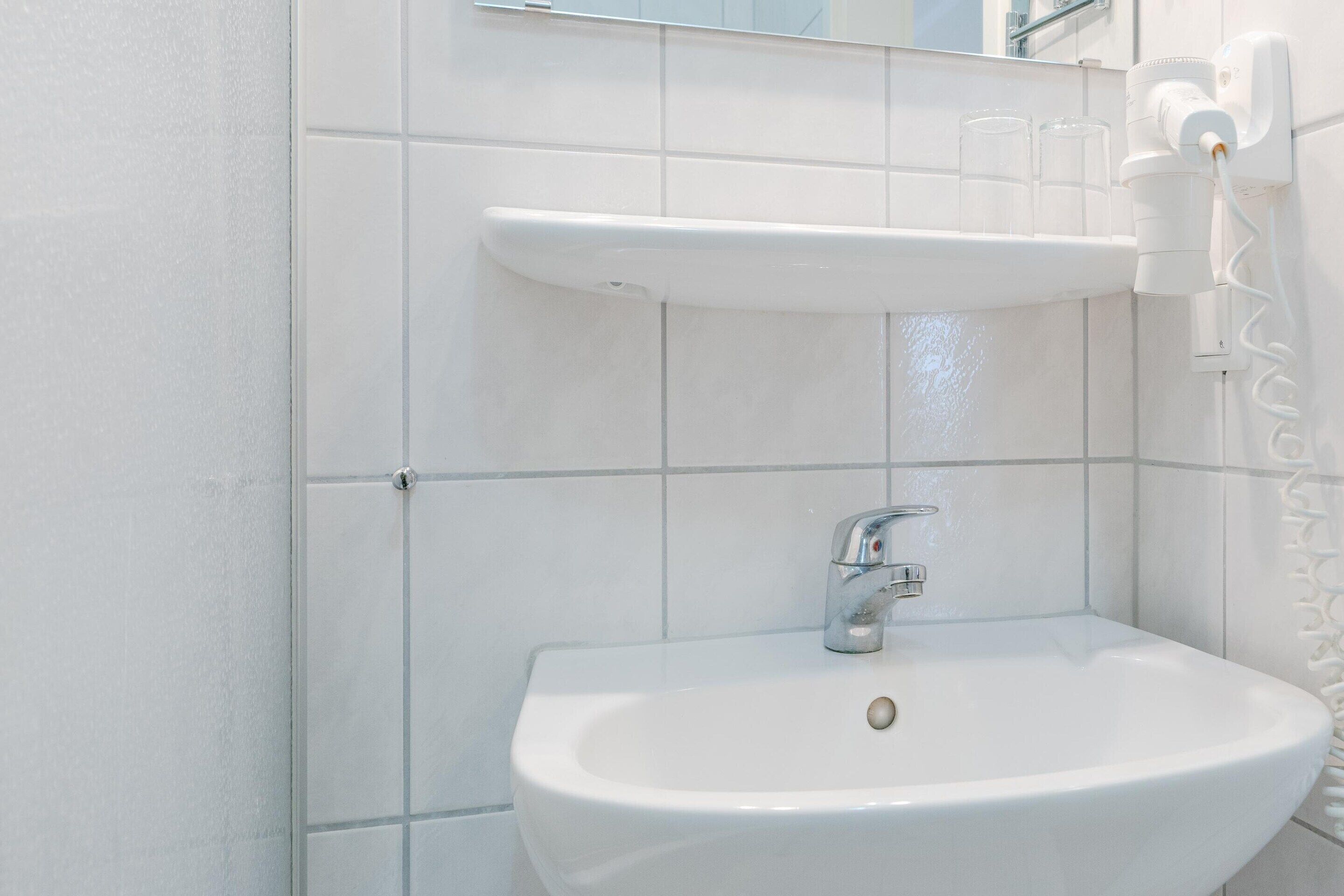 Un baño con lavamanos blanco, espejo y dispensador de toallas.