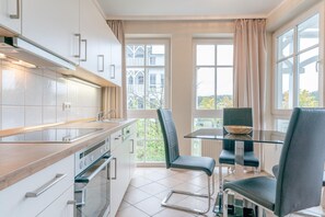 Eine moderne Küche mit weißen Schränken, einer Holztischplatte und einem Glastisch mit zwei Stühlen.
